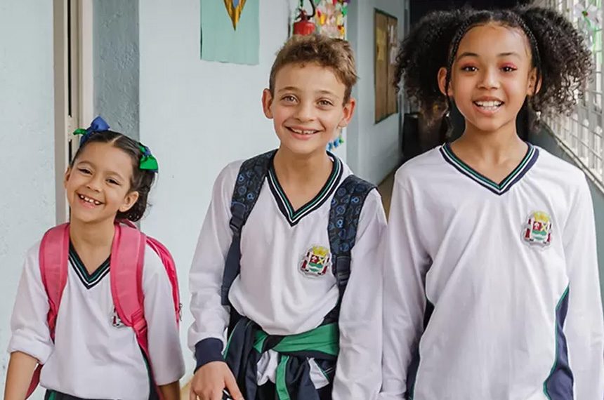 alunos-sorrindo-chegando-na-escola-andando-pelo-corredor-com-mochilas-e-materiais